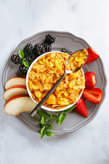 Fruit and cornflakes breakfast. Fresh apples, berries and strawberry with healthy flakes in a bowl from above. Rich and healthy eating concept. Top view