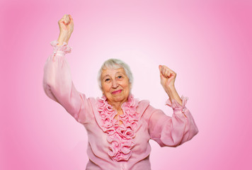 portrait of a cheerful senior woman gesturing victory over pink