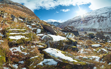 Norwegian mountain landscape. Snow covering mossy rocks, distant mountain flow and sun shining.