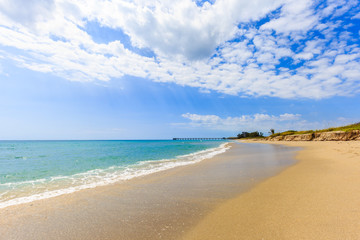 Fototapeta na wymiar Beautiful sandy beach with blue sky, green sea and wood bridge pier.