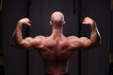 Young healthy bald ripped man with big muscles posing in gym, view from the back