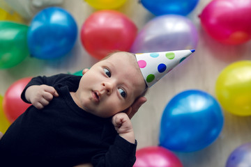 Fototapeta na wymiar child in a festive cap in polka-dot lies on his hands against the background of colorful balloons