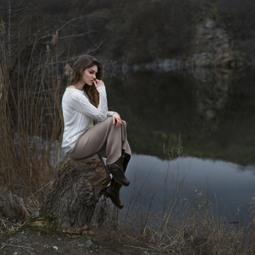 Pensive Caucasian woman sitting on tree stump at river