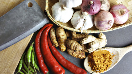 Asian cuisine ingredients of herbs, spices, turmeric, red pepper, green pepper, knife, garlic and shallots. on a black background. View from the Top