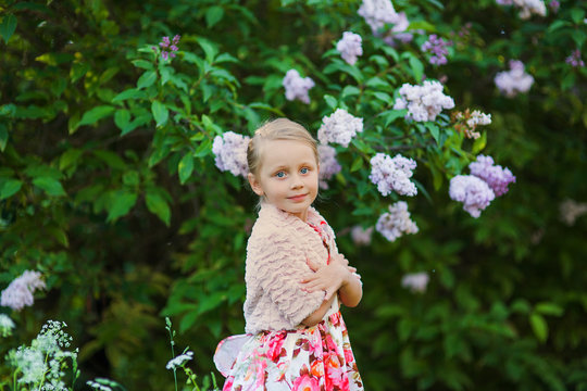 Portrait of cute blonde girl in park with lilac trees in the summer day