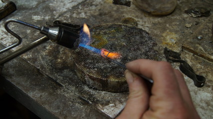 The jeweler heats the precious metal with a gas burner.