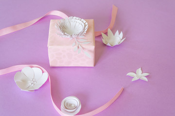 Pink gift with white paper flowers and pink ribbon on pink background. Cut from paper.