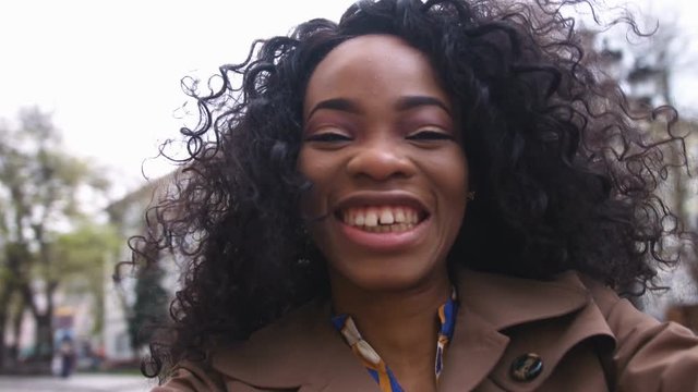 Portrait of a beautiful young afro american woman with curly hair turns the camera smiling, happy feeling in the city center