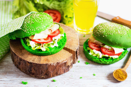 Fast food, barbecue, vegetarian burger with a green bun with sesame, fresh cucumber, tomato, lettuce, cheese mayonnaise and spices, with a glass of juice on a white rustic wooden background