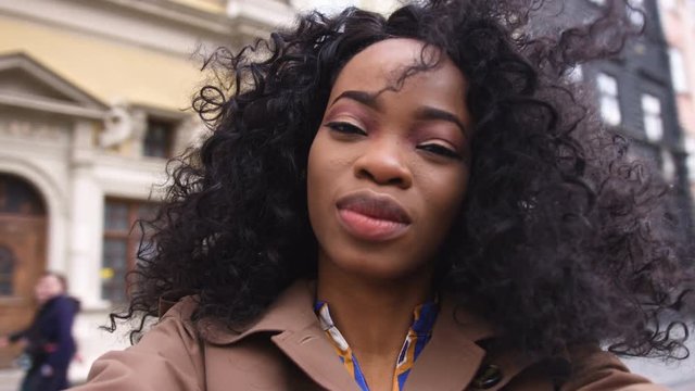 Portrait of a beautiful young afro american woman with curly hair turns the camera smiling, happy feeling in the city center