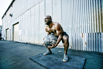 Black man lifting heavy ball outdoors