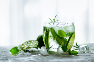 Homemade lime lemonade with cucumber, rosemary and ice, white background. Cold beverage for hot summer day. Copyspace.