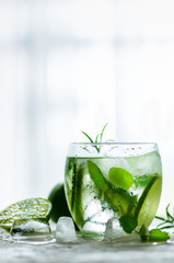 Homemade lime lemonade with cucumber, rosemary and ice, white background. Cold beverage for hot summer day. Copyspace.