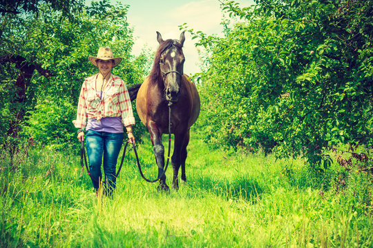 Western woman walking on green meadow with horse