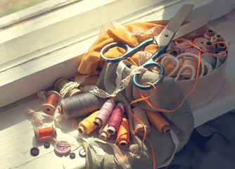 Old scissors, spools of thread, fabric and buttons illuminated by the sun. 