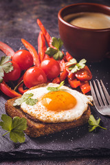 Toast with fried egg and vegetables and coffee on dark stone background