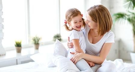 Happy family mother and child daughter laugh in bed.