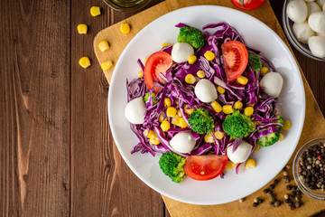 Fresh vegetable salad with mozzarella on wooden table. © nesavinov