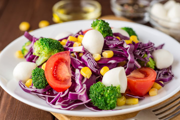 Fresh vegetable salad with mozzarella on wooden table.