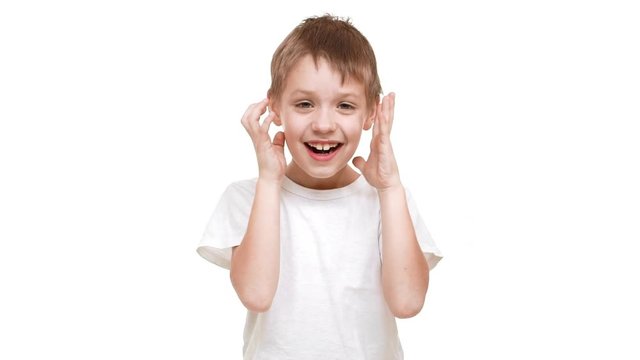 Young Caucasian boy standing on white background with face covered with hands. Then opening and trying to scare in slowmotion