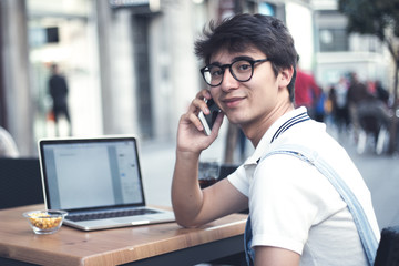 Young man using mobile phone in the city of Madrid. Young boy in the heart of madrid. Madrid centro. Hipster and student lifestyle. Wearing vintage clothes. Student boy sitting in a bar with mobile p 