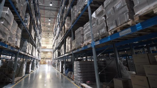 Large warehouse logistics terminal. Camera moves up on shelves of cardboard boxes inside a storage warehouse. Industrial warehouse with boxes