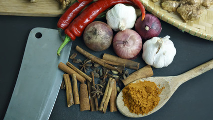 cinnamon, curry powder, garlic, onion, chili, meat cleaver on a black background, Concept cuisine Asian countries.