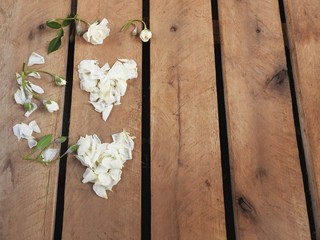 Dois corações um sobre o outro formados de pétalas de rosas brancas, alguns botões de rosa como enfeite ao lado sobre paletes de madeira rústica