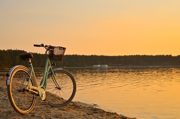 Fototapeta premium Vintage bicycle with a basket near the lake during beautiful summer sunset. Copy space.