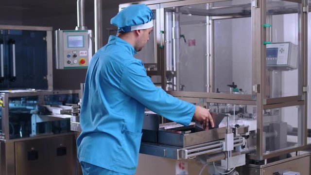 Factory operator control pharmaceutical packaging machine. Pharmaceutical manufacturing process. Pharmaceutical worker take packaging from manufacturing line. Pharmaceutical factory. Pharmacy factory