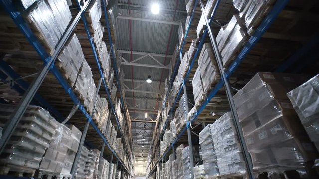 Large warehouse logistics terminal. Camera moves up on shelves of cardboard boxes inside a storage warehouse. Industrial warehouse with boxes