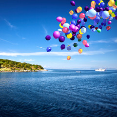 Colorful balloons drifting over the calm blue sea.
