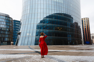 Young beautiful glamorous blonde girl in a red dress posing near glass showcase in business center. Wide photo.