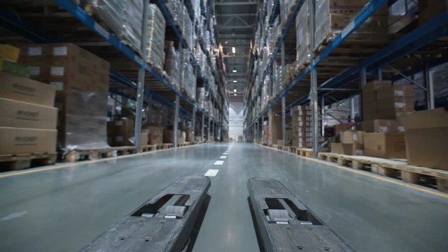 Forklift trucks move between large metal shelves at a modern warehouse. Large warehouse logistics terminal. moves up on shelves of cardboard boxes inside a storage warehouse. Industrial warehouse