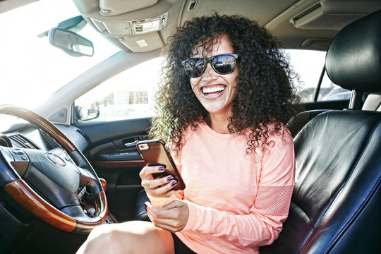 Laughing Hispanic woman in car holding texting on cell phone - Powered by Adobe