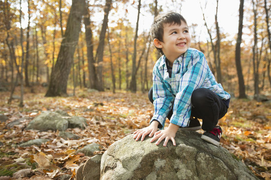 Smiling Mixed Race boy crouching on rock in autumn