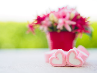 Closeup of sweet marshmallow in the shape of heart on wooden plate and flower at background. Concept about love and relationship. (Soft Style for Background)