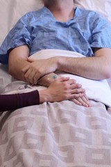 Women holding a patients hand while he is laying in the hospital bed 