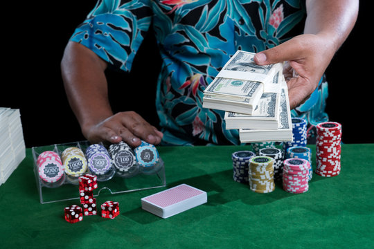 Banknote in hand and chips with casino devices on green table