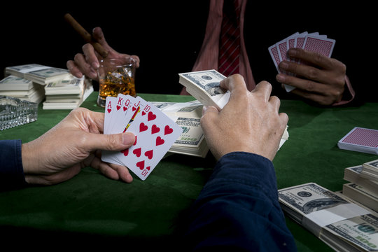 The gambler is putting bets into the piles of banknote and holding straight flush in a hand