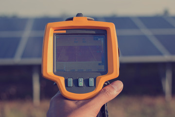 engineer or electrician working on  maintenance equipment at solar power plant;  engineer using thermal imager to check temperature heat of solar panel 