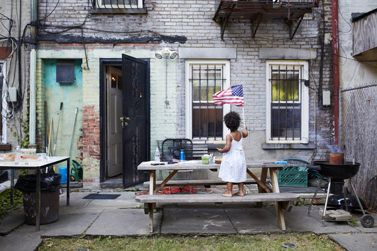 Girl waving American flag while standing on bench at backyard
