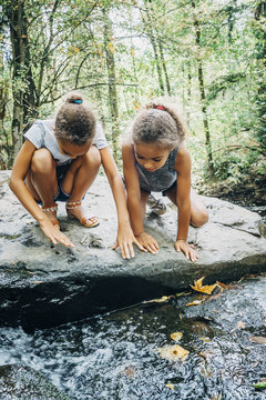 Mixed Race girls kneeling on rock looking at stream
