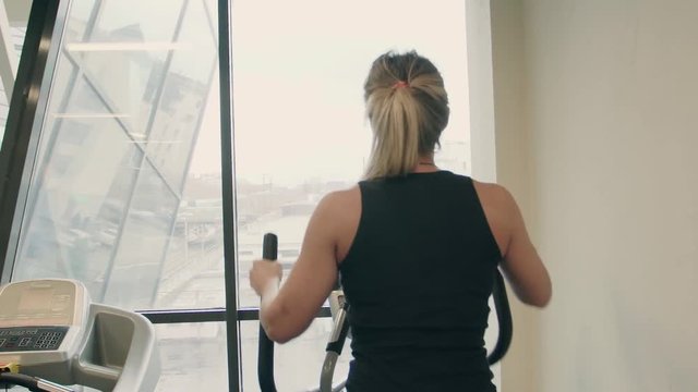 pretty 20s woman in sportswear in working on ellipsoid machine in a gym