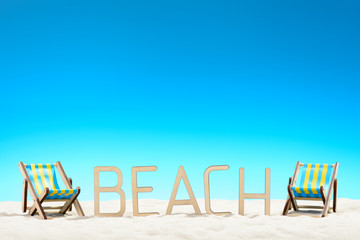 The word BEACH and two sunbeds at the beach on background of blue sky