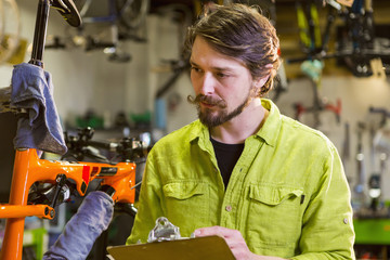 Caucasian worker writing on clipboard in bicycle shop