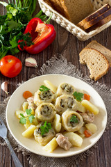 Potatoes stewed with meat and rolls of dough with garlic and greens in a plate on the kitchen table. Noodle is a national dish of Ukrainian cuisine.