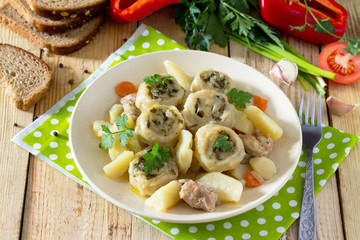Potatoes stewed with meat and rolls of dough with garlic and greens on a wooden table, served with fresh vegetables. Nudley is a national Ukrainian dish.