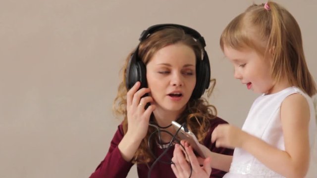 A young mother with a little daughter listening to music on the phone with headphones
