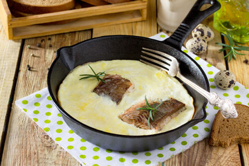 Omelette with red fish in a cast-iron frying pan on a wooden table. The concept of a healthy diet and diet.